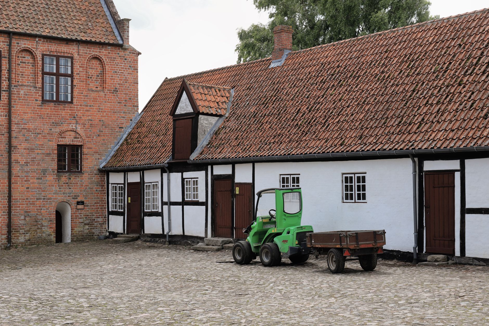 Gammel gård med bindingsværk og en lille traktor i gården